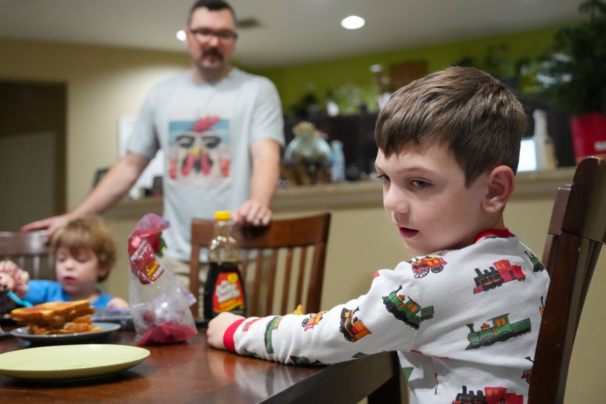 Henry Herzog, 7, watches his sister play with a family dog as he eats breakfast on Monday, March 9, 2026, at their home in Manvel.