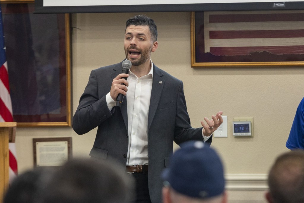 A man in a suit holding a microphone in a meeting room.